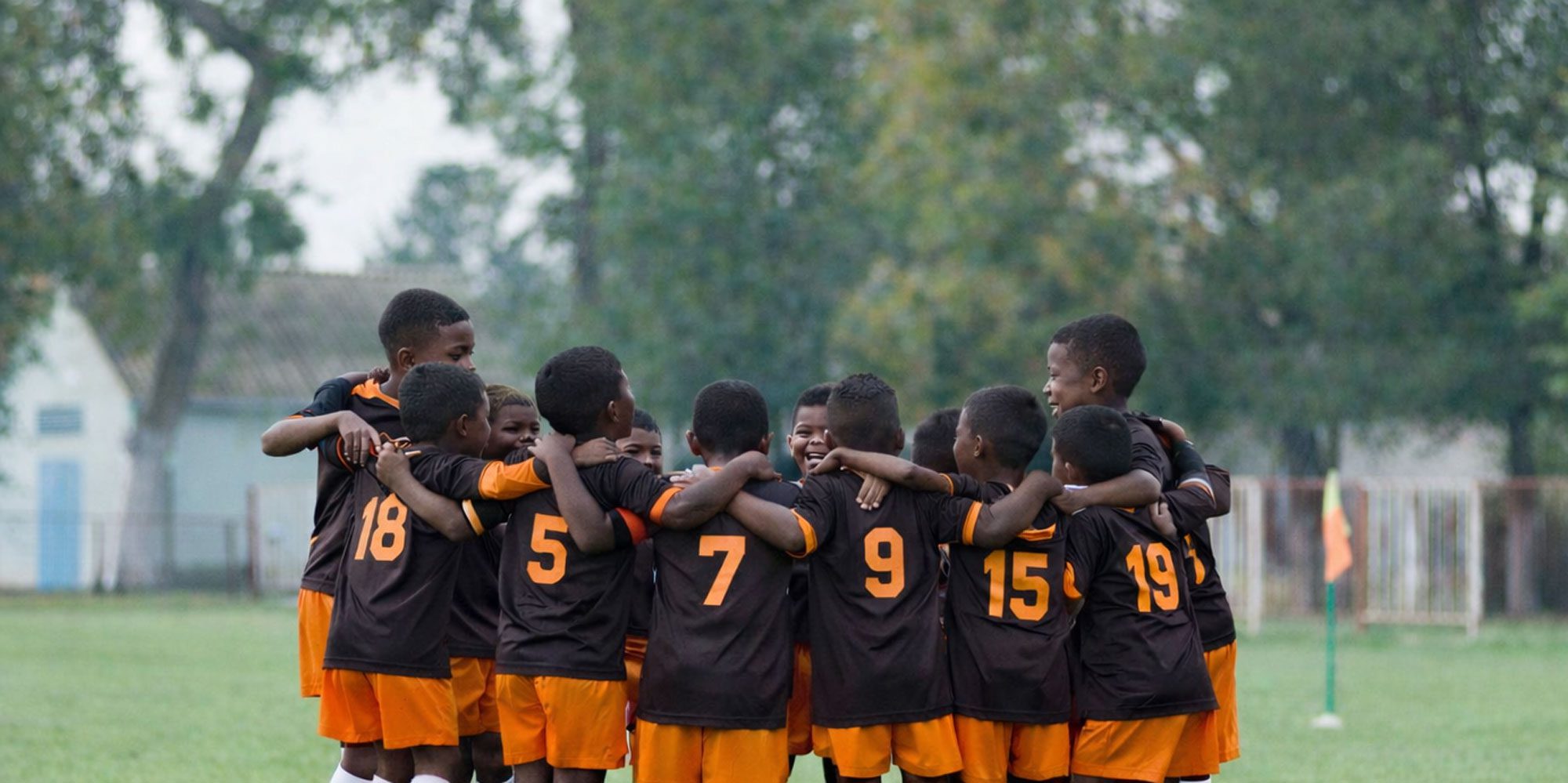 Boys' soccer team in black and orange uniforms huddled on a field.